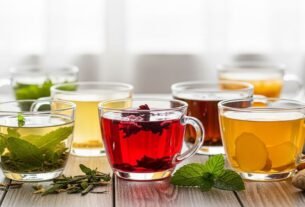 Uma coleção convidativa de três chás para emagrecer quentes – hibisco, chá verde e gengibre – dispostos em copos de vidro sobre uma mesa de madeira clara. A cena transmite tranquilidade, bem-estar e o poder natural dos chás para uma vida saudável.