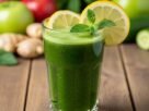 Um copo de sucos detox verde vibrante, decorado com limão e hortelã, cercado por ingredientes frescos como maçãs, gengibre e pepino